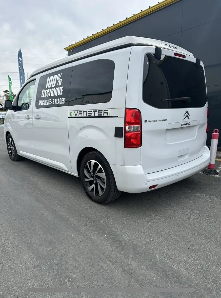 Vue 3/4 arrière droite d'un Citroën Jumpy van blanc électrique avec marquage "100% électrique" et jantes alu 17 pouces.