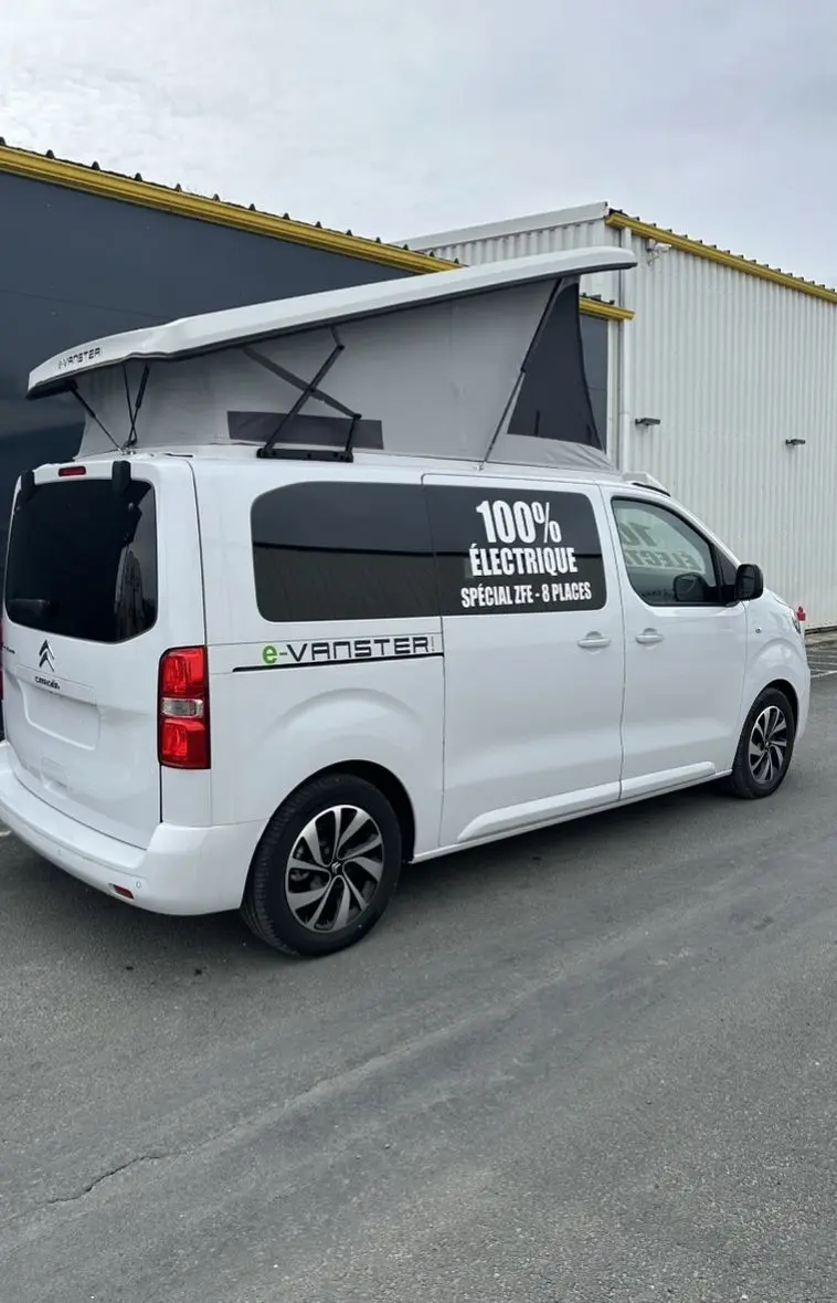 Vue 3/4 arrière droite du Citroën Jumpy blanc avec toit relevable et marquage "100% électrique" sur la vitre latérale.