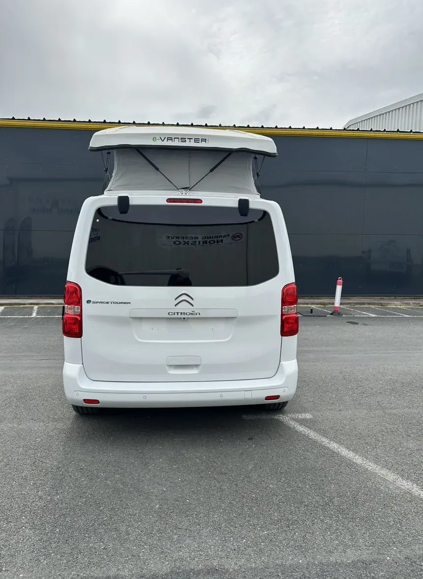 Vue arrière d'un Citroën Jumpy van blanc électrique avec toit relevable e-Vanster déployé sur parking.
