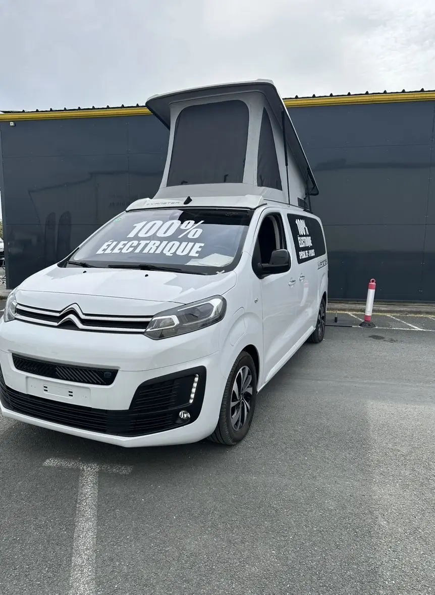 Vue 3/4 avant droit d'un Citroën Jumpy van blanc électrique avec toit relevable et marquage "100% électrique" visible.