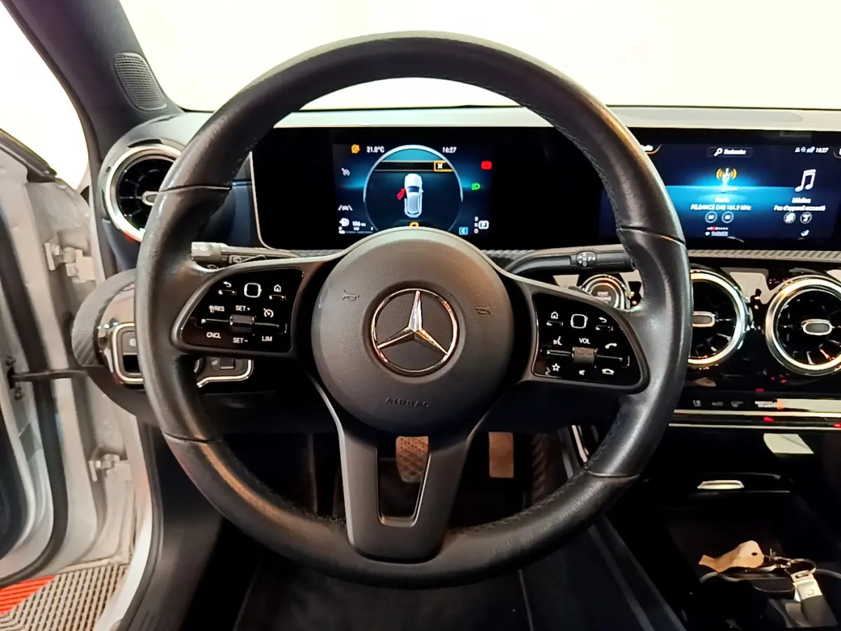 Vue rapprochée du volant cuir noir et du tableau de bord numérique d'une Mercedes Classe A gris clair 2020.