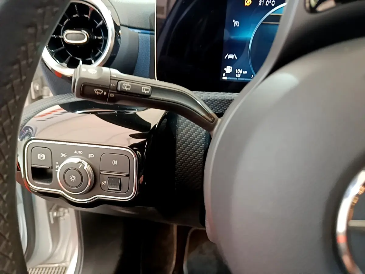 Gros plan sur le tableau de bord côté gauche d'une Mercedes Classe A gris clair, avec commandes d'éclairage et volant partiel visible.