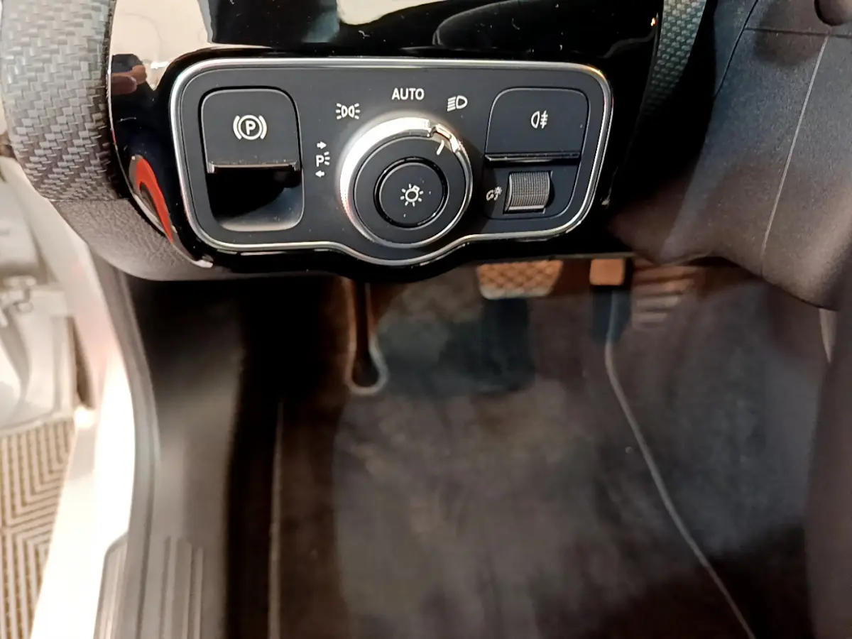 Gros plan sur les commandes d'éclairage et frein à main électrique côté gauche dans l'habitacle d'une Mercedes Classe A gris clair.