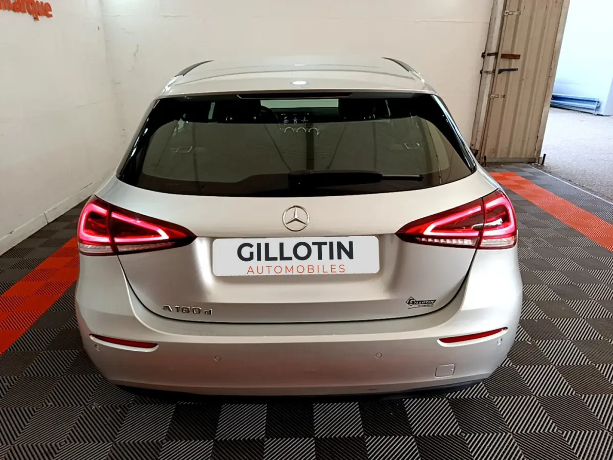 Vue arrière d'une Mercedes Classe A 180 d Business Line gris clair avec feux LED allumés en intérieur showroom.