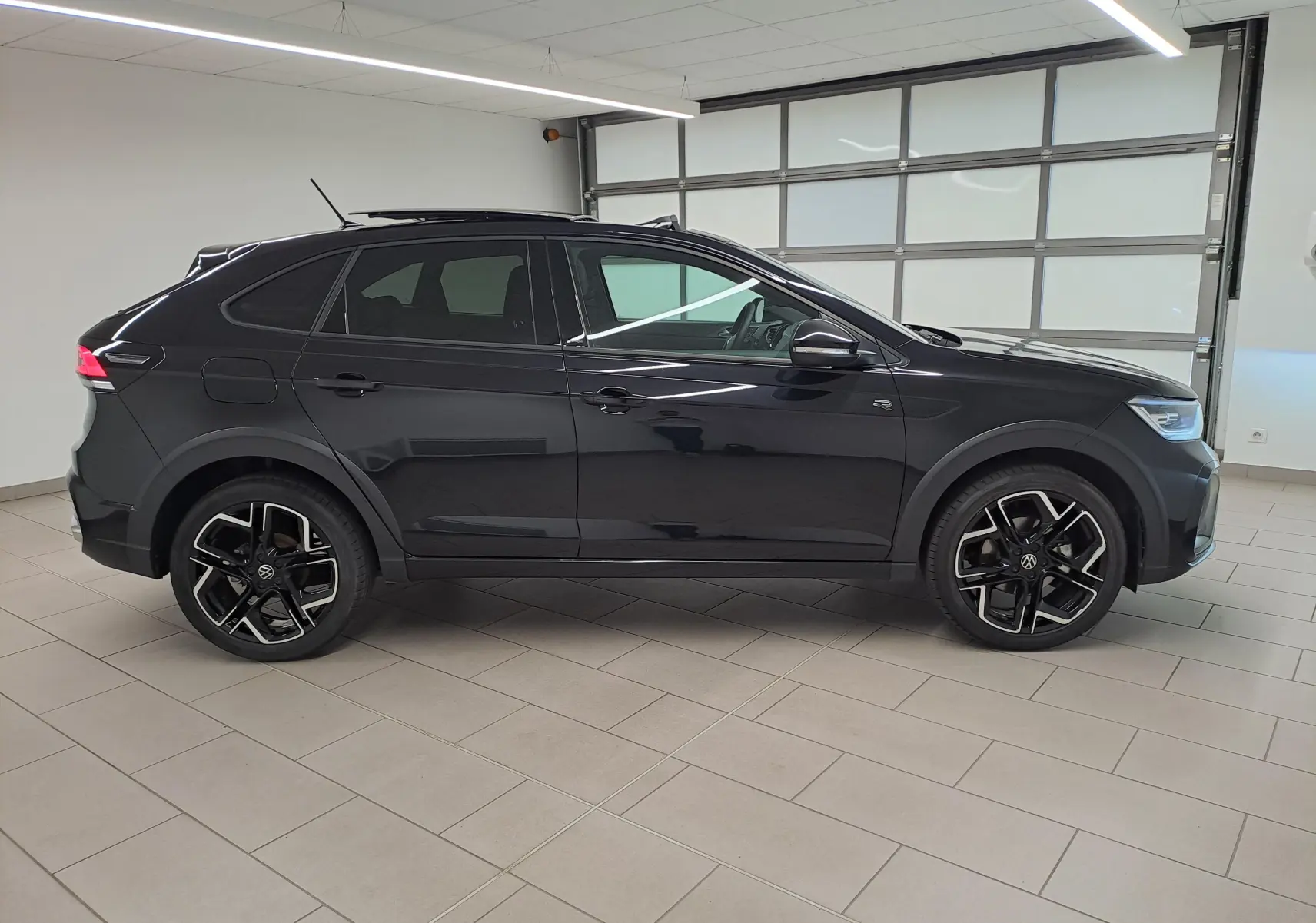 Vue de profil côté gauche d'un Volkswagen Taigo noir intense nacré avec jantes alliage R-Line dans un showroom.