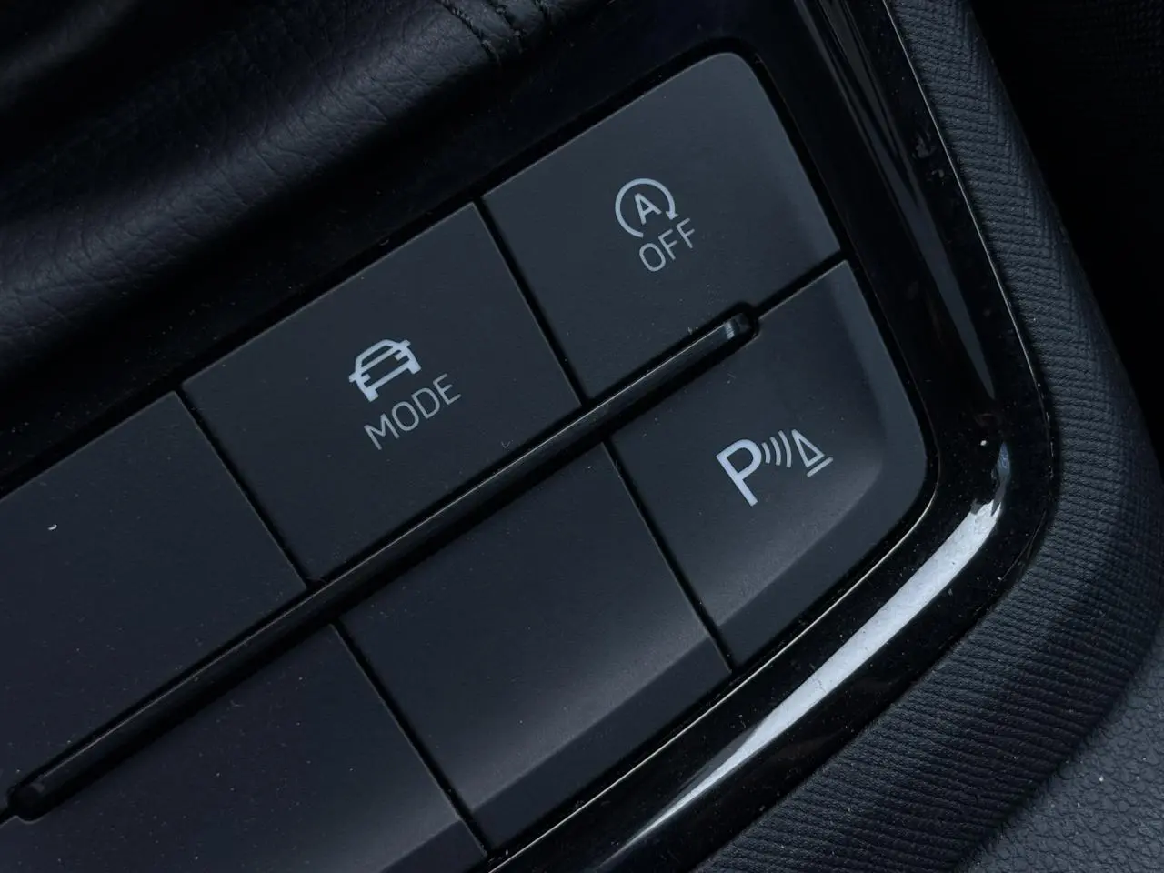 Gros plan sur les boutons de commande du mode de conduite et du stationnement assisté dans une Skoda Scala gris reflex.