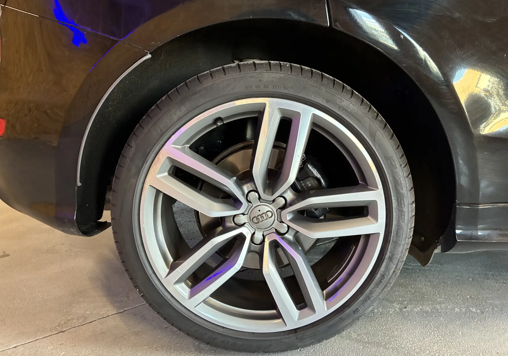 Gros plan sur la jante alu avant droite d’un Audi SQ5 noir, mettant en valeur le design sportif et le logo Audi central.