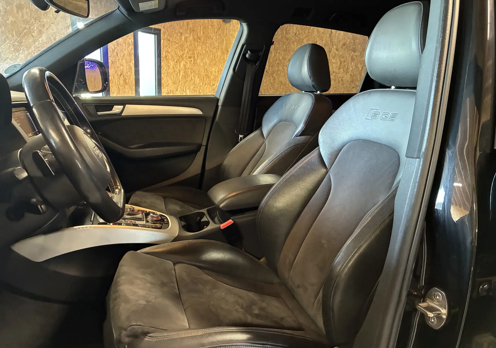 Vue intérieure côté conducteur de l'Audi SQ5 noir, sièges sport en cuir avec logo SQ5 embossé sur appuie-tête.