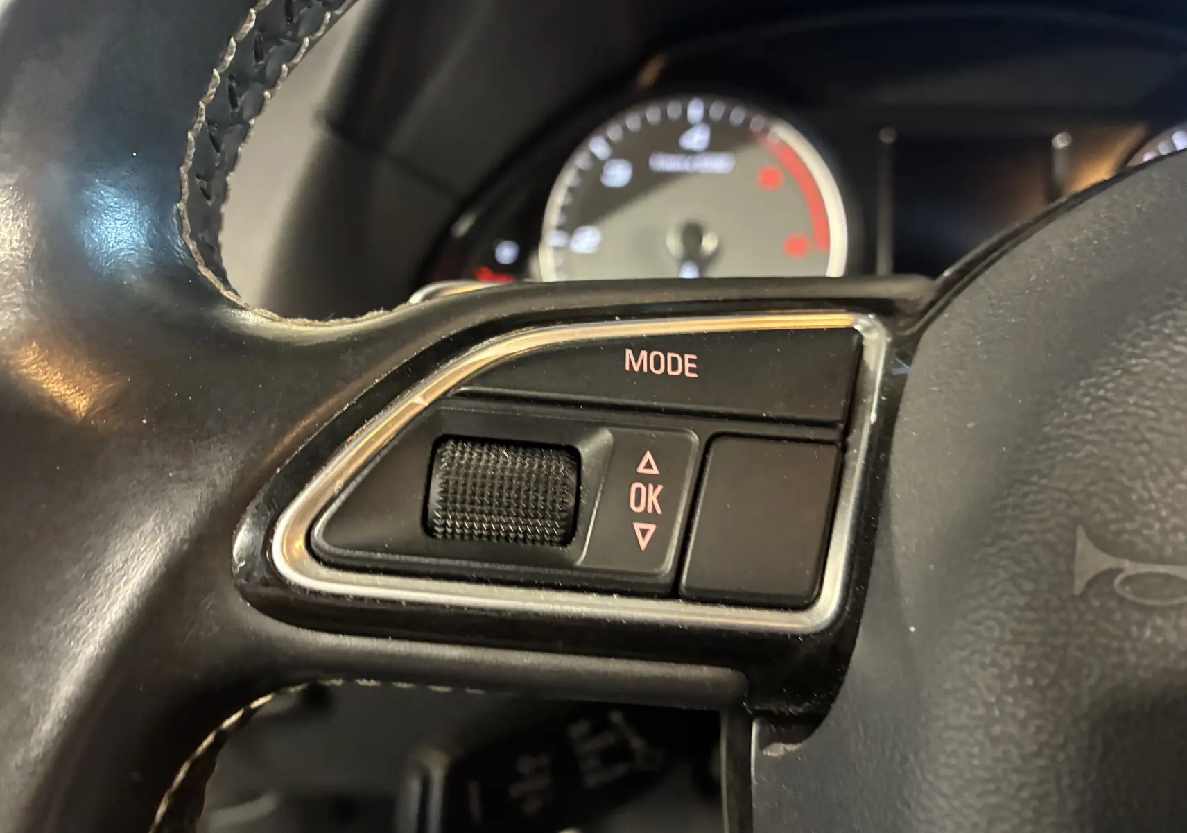 Gros plan sur les commandes mode et OK du volant cuir noir de l'Audi SQ5 2016, avec tableau de bord flou en arrière-plan.