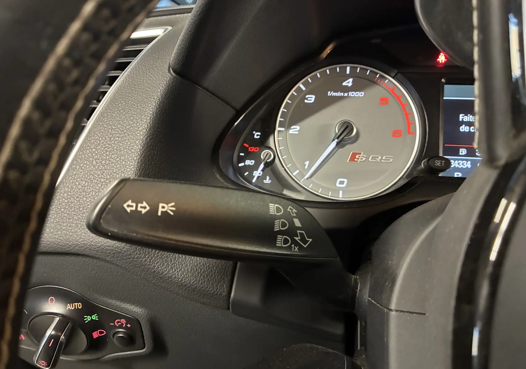 Gros plan sur le compte-tours gris et le commodo de clignotants de l'Audi SQ5 noir, vue depuis le volant.