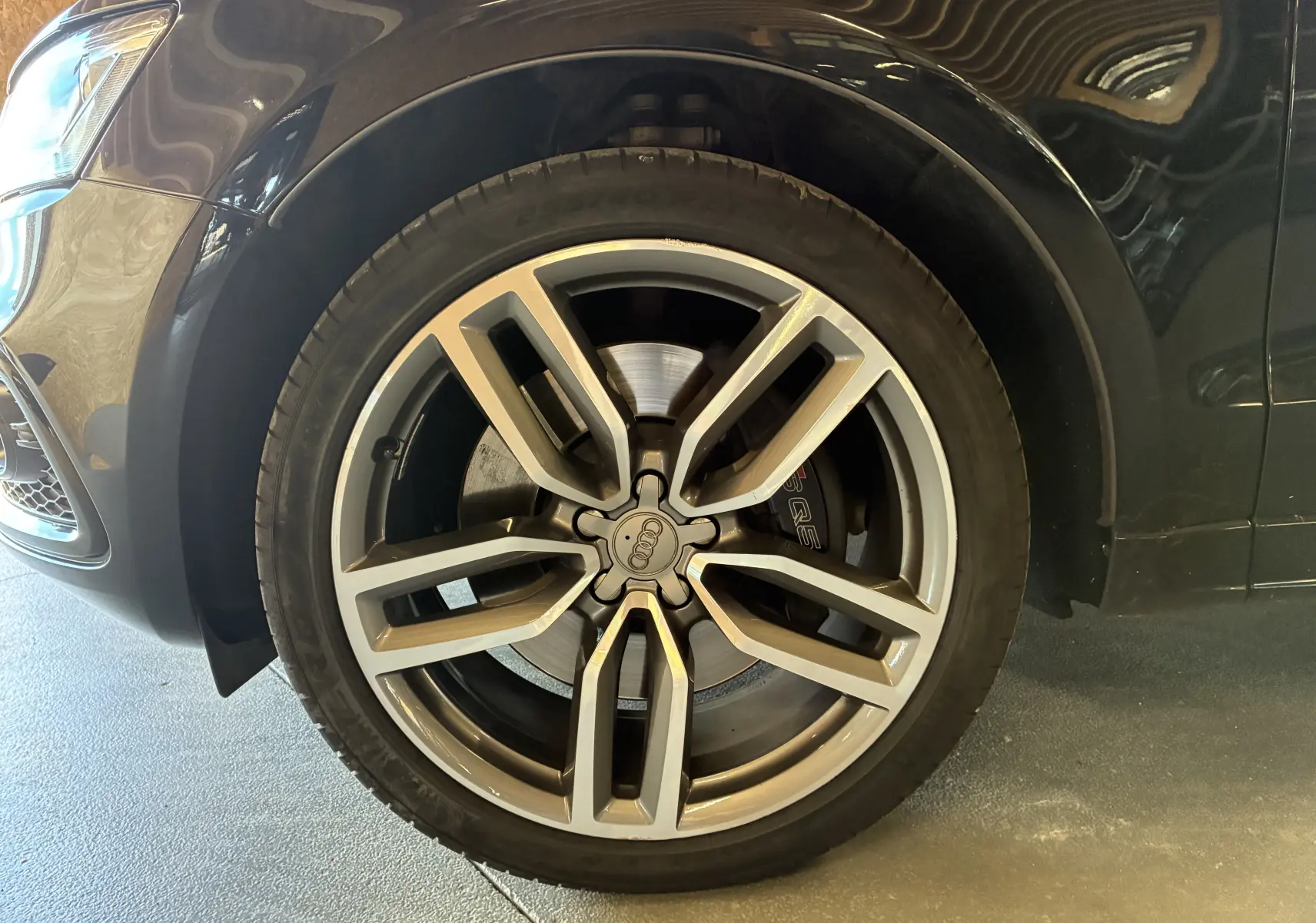 Gros plan sur la roue avant gauche d’un Audi SQ5 noir, avec jante alu à cinq branches doubles et logo Audi central.