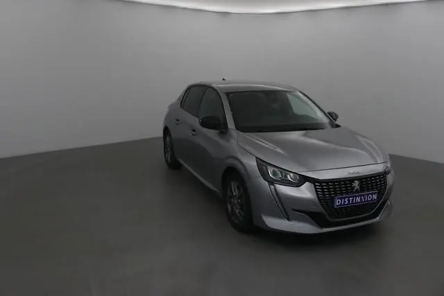 Peugeot 208 gris Artense vue 3/4 avant droit dans un studio, calandre noire et feux LED distinctifs visibles.