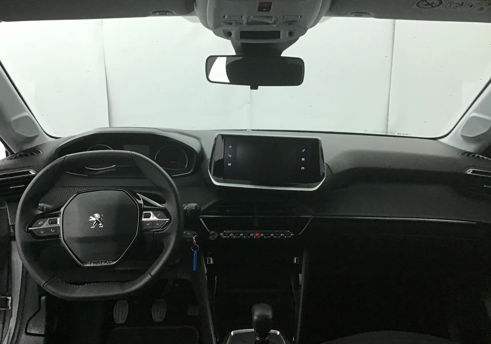 Intérieur de la Peugeot 208 2022 vue de face, tableau de bord noir avec écran tactile central et volant compact griffé Peugeot.