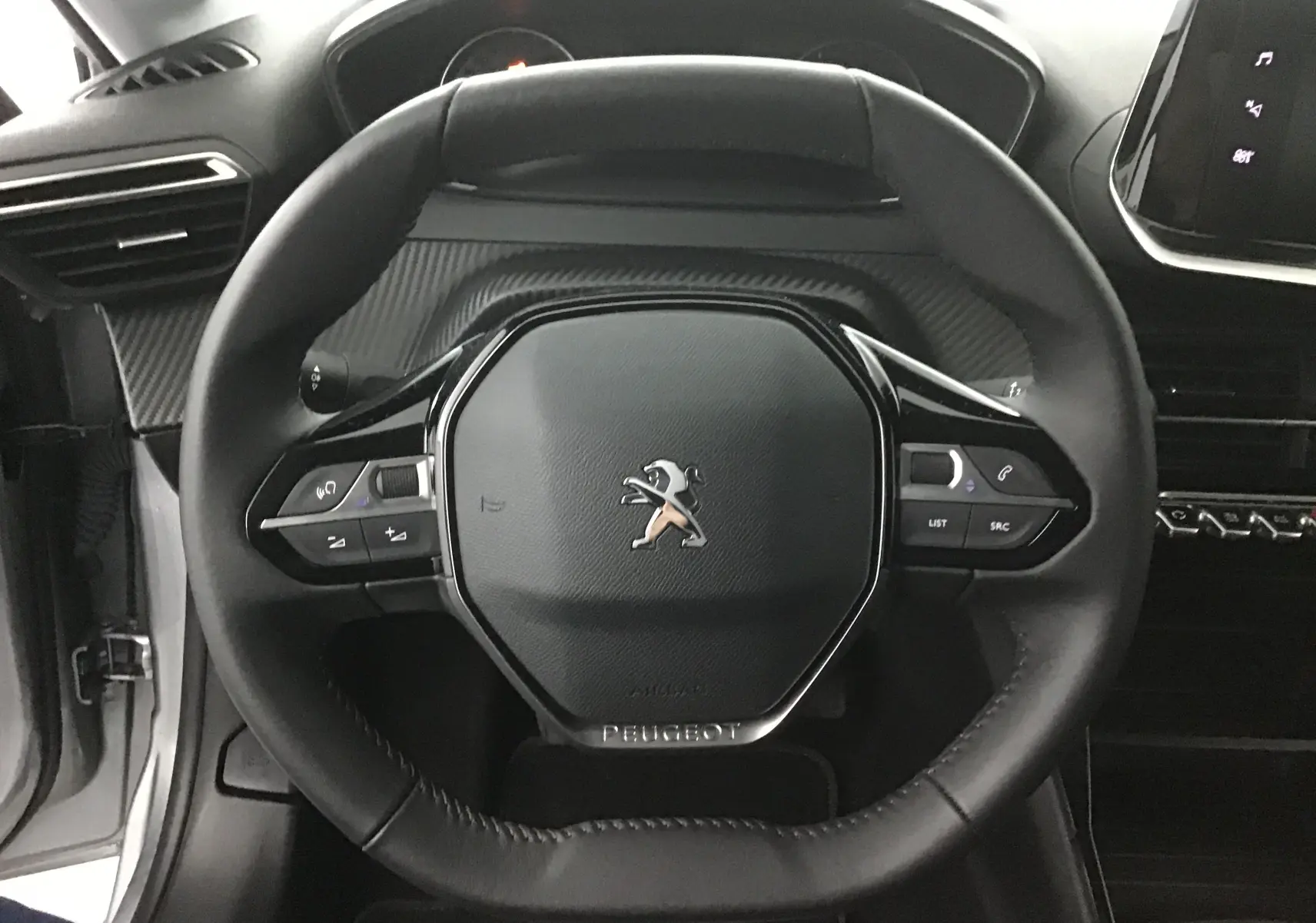 Vue rapprochée du volant cuir noir de la Peugeot 208 gris Artense, avec commandes intégrées et tableau de bord partiel visible.