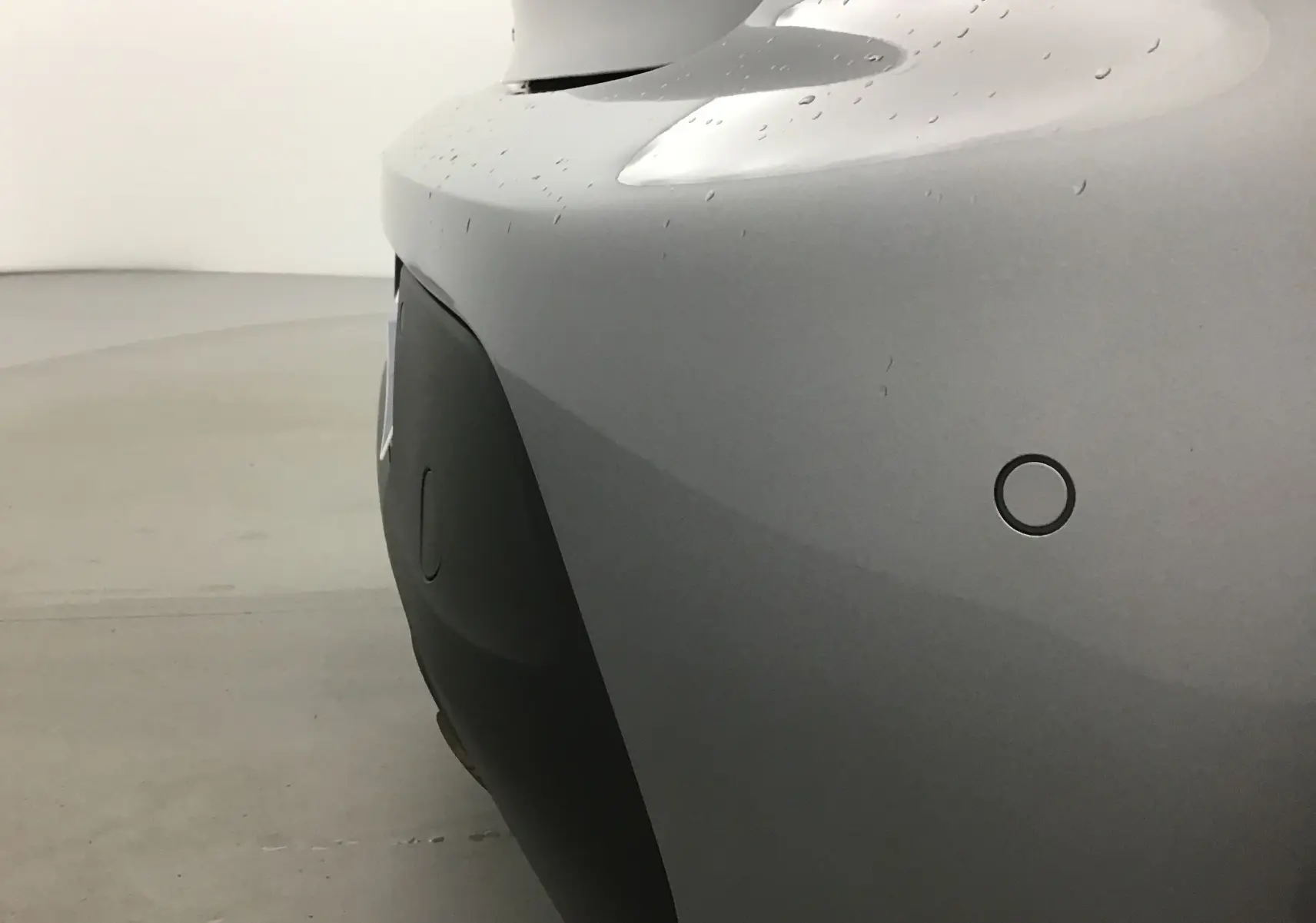 Gros plan sur le pare-chocs arrière gris Artense d'une Peugeot 208 2022 avec capteur de stationnement circulaire visible.