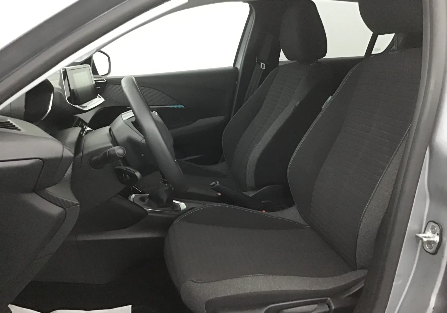 Vue intérieure côté conducteur de la Peugeot 208 2022 gris Artense, sièges tissu noir et tableau de bord moderne.