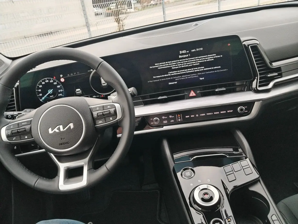 Vue intérieure du tableau de bord et volant KIA Sportage 2025, avec écran tactile large et commandes au volant.
