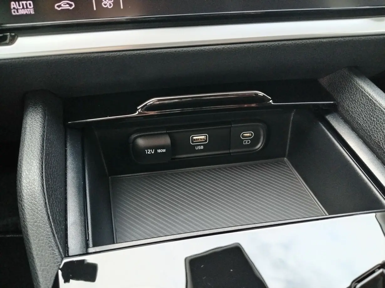 Gros plan sur la console centrale du Kia Sportage 2025, montrant les ports USB et prise 12V dans un intérieur noir.