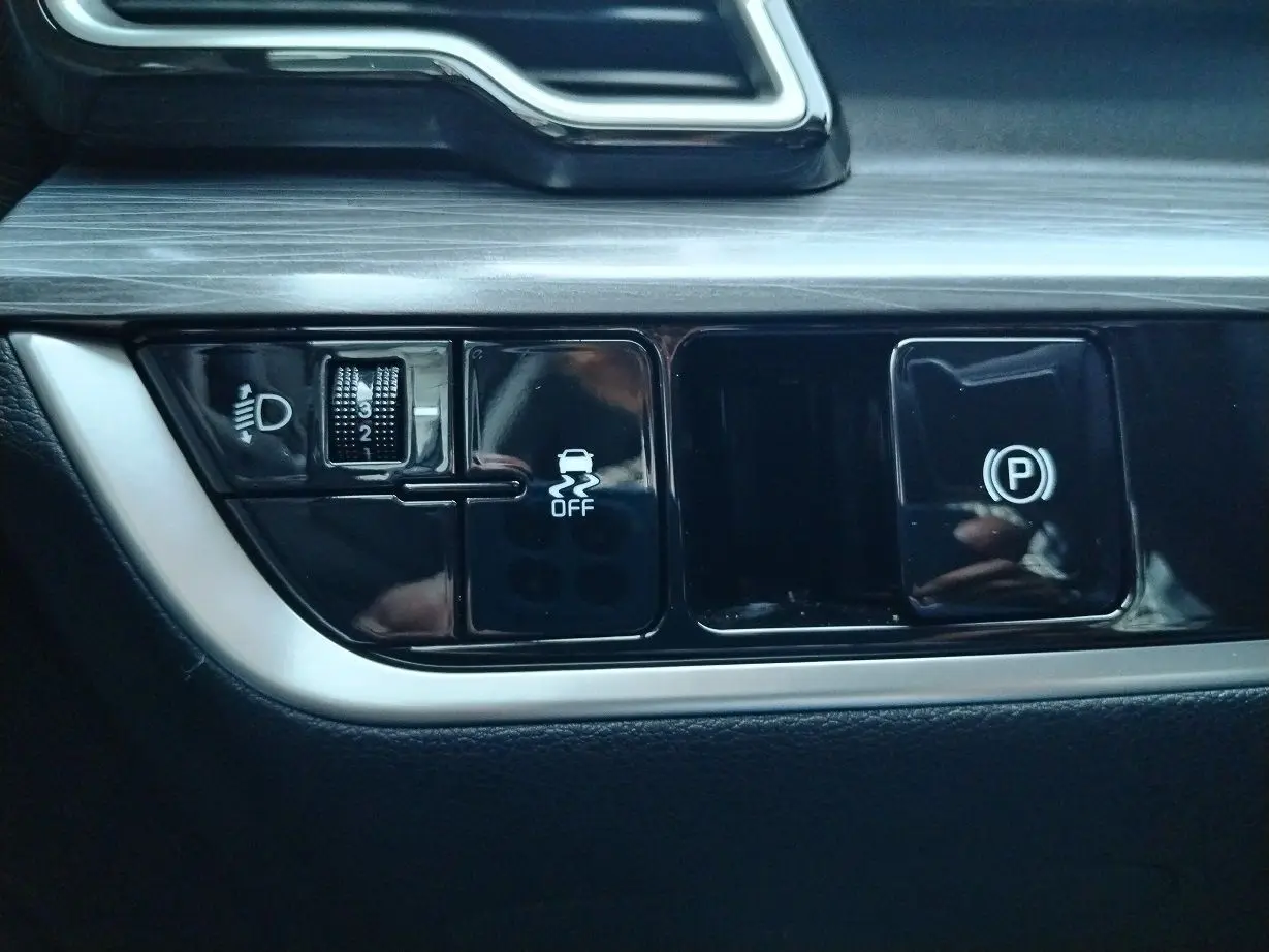 Gros plan sur les commandes noires du tableau de bord du Kia Sportage 2025, avec réglage des phares et frein de stationnement.