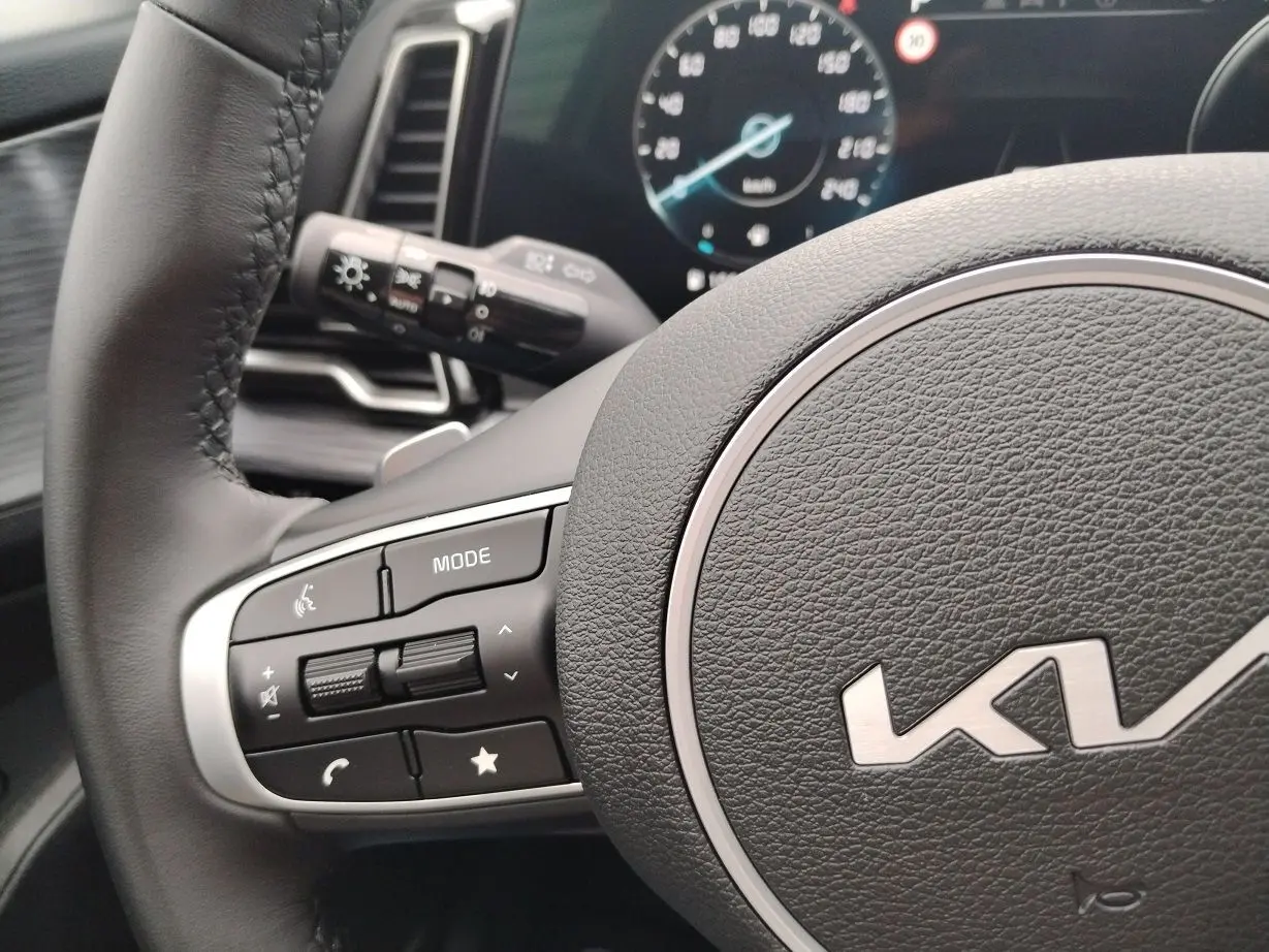 Gros plan sur le volant noir du Kia Sportage 2025 avec commandes intégrées et tableau de bord numérique en arrière-plan.