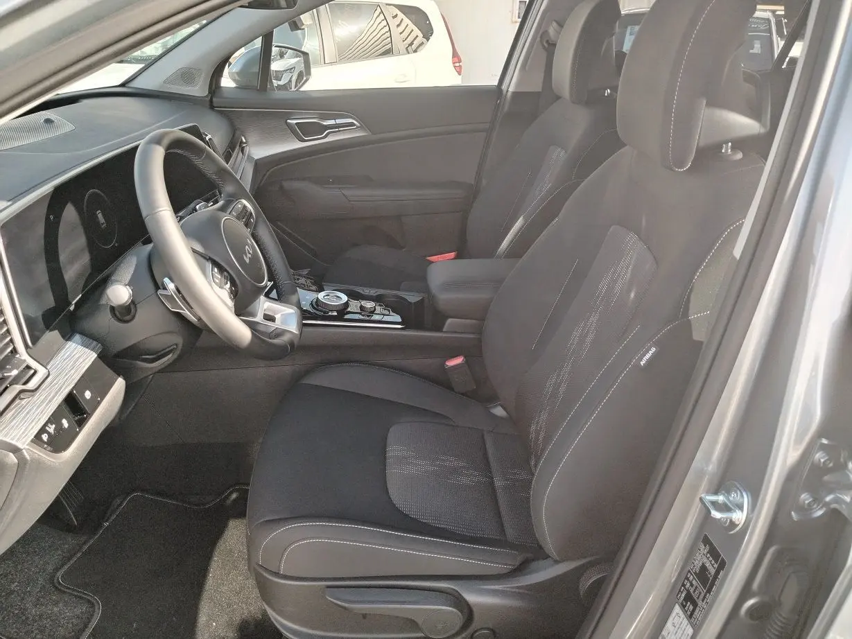 Vue intérieure côté conducteur du Kia Sportage gris perle 2025, avec sièges noirs et tableau de bord moderne.