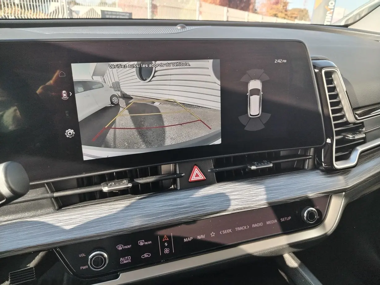 Écran central du Kia Sportage 2025 montrant la caméra de recul avec vue arrière et lignes de guidage jaunes et rouges.