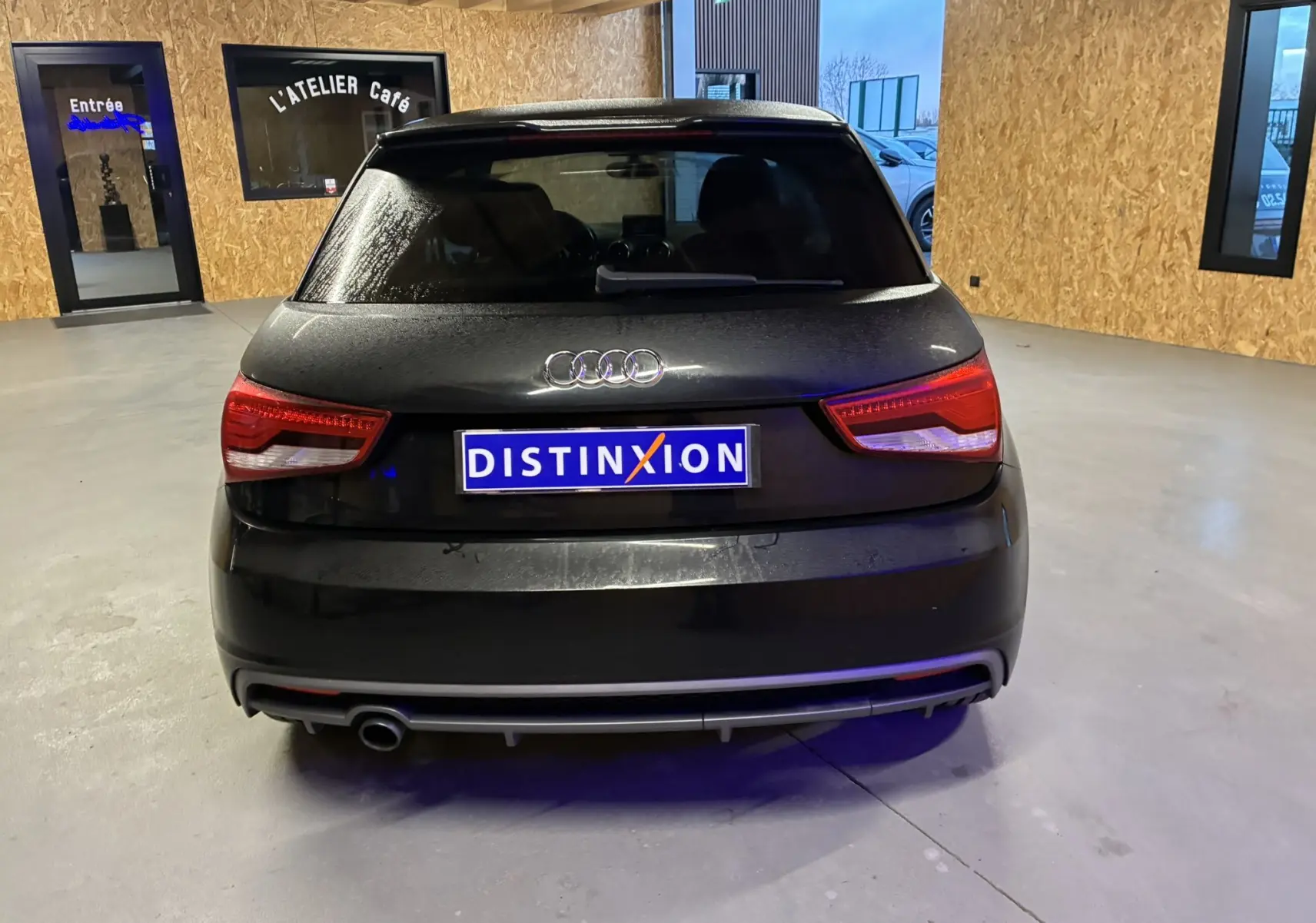 Vue arrière d'une Audi A1 noire de 2016, avec feux rouges allumés et plaque Distinxion visible en intérieur.