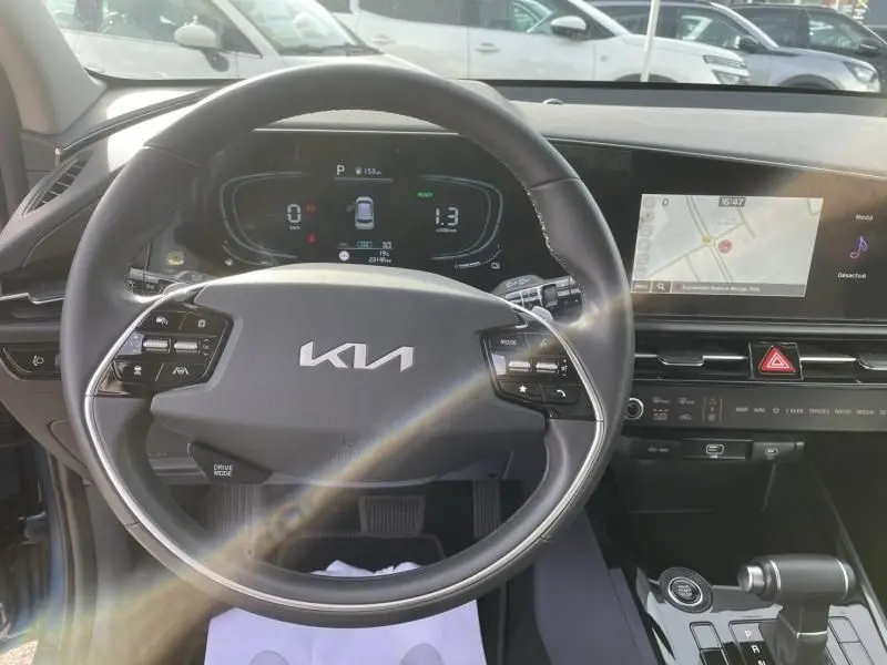 Vue intérieure centrée sur le volant du KIA Niro bleu métal 2024, avec tableau de bord numérique et écran tactile de navigation.