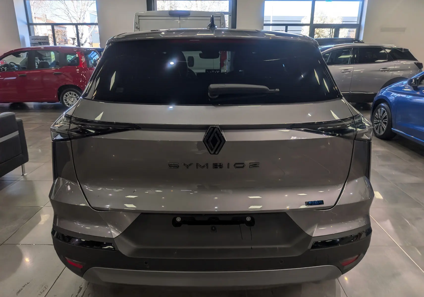 Vue arrière d'une Renault SYMBIOZ gris Cassiopé avec logo central et feux arrière fins en intérieur showroom.
