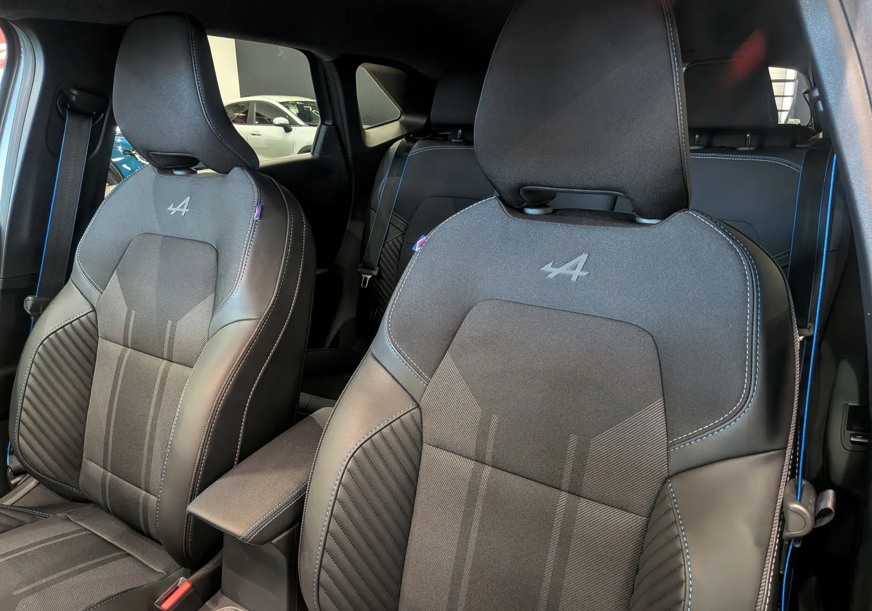 Vue intérieure rapprochée des sièges avant noirs avec surpiqûres bleues et logo Alpine sur le Renault Symbioz 2026.