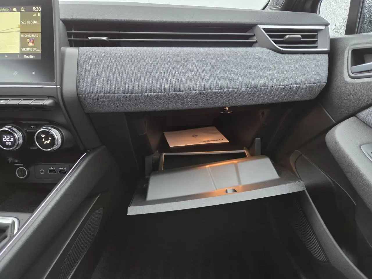 Intérieur avant droit de la Renault Clio 2025 gris schiste, tableau de bord avec boîte à gants ouverte et écran tactile visible.