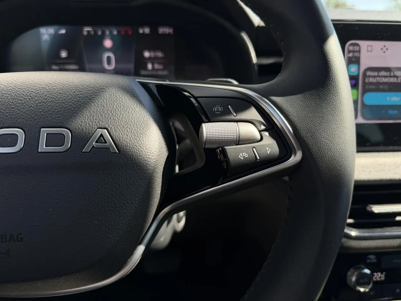 Gros plan sur le volant cuir noir du Skoda Scala 2025, avec commandes multifonctions et tableau de bord numérique flou en arrière-plan.