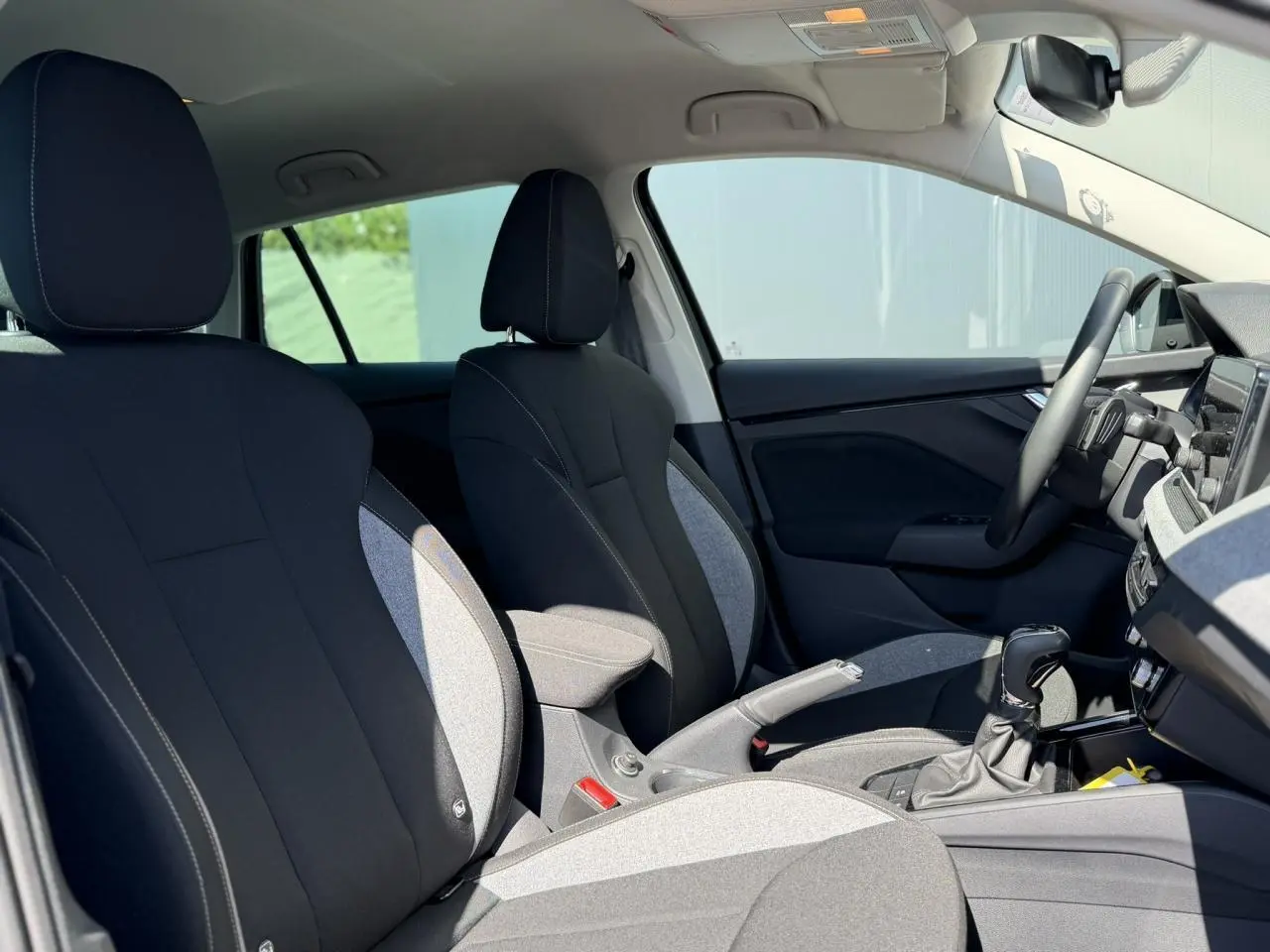 Intérieur avant de la Skoda Scala 2025, vue côté droit, sièges bi-ton gris et noir avec accoudoir central.