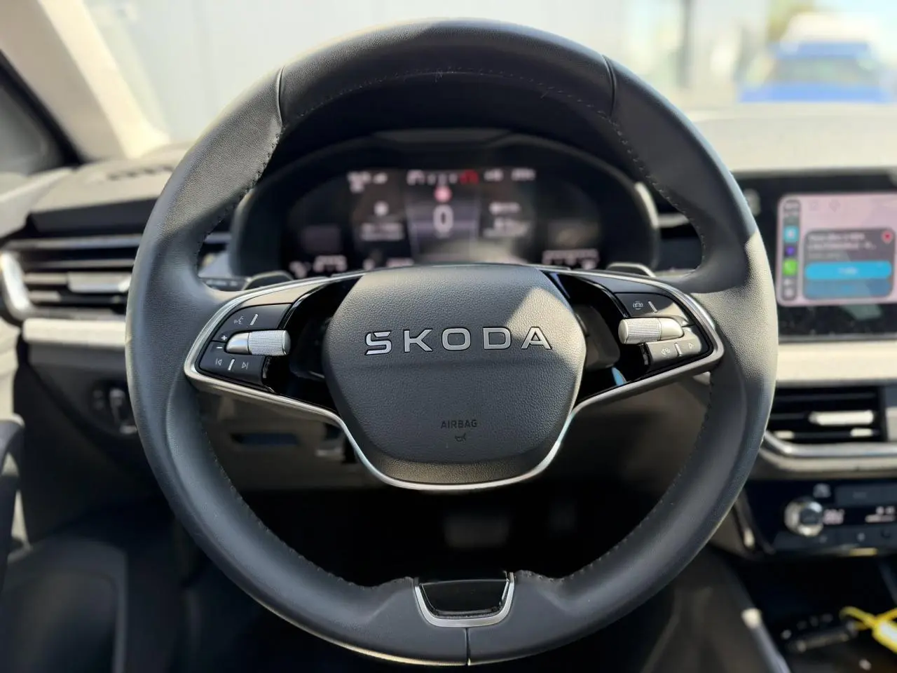 Gros plan sur le volant cuir multifonctions SKODA d'une SCALA 2025, avec tableau de bord numérique en arrière-plan flou.