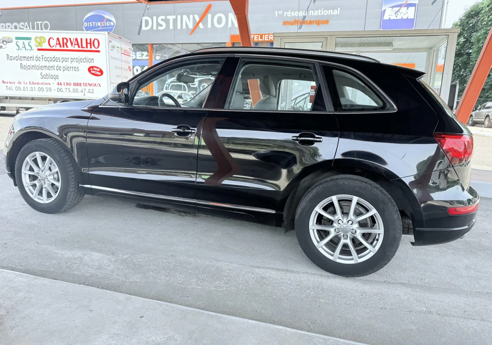 Audi Q5 noir vue de profil côté gauche, stationné sous un abri avec jantes argentées visibles.