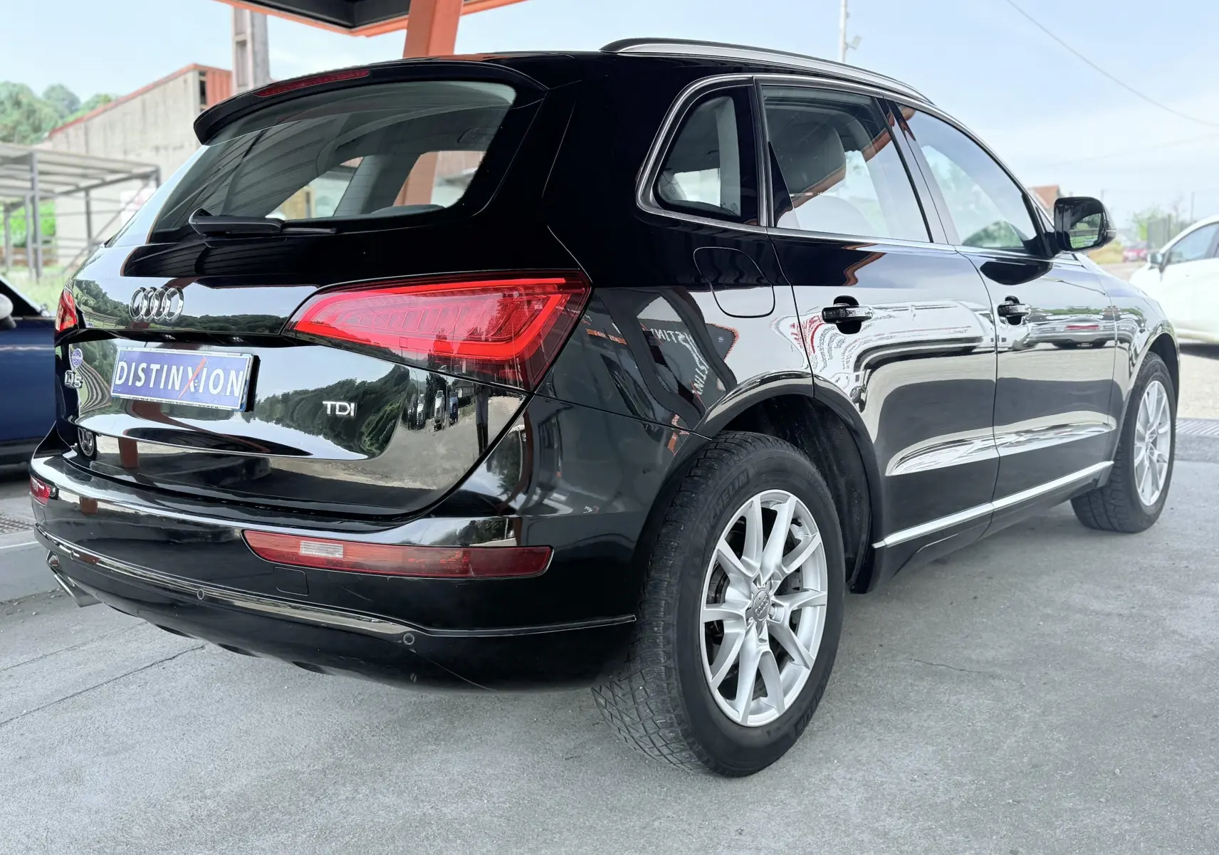 Audi Q5 noir vue 3/4 arrière droit, avec jantes alliage et feux arrière allongés sous abri.