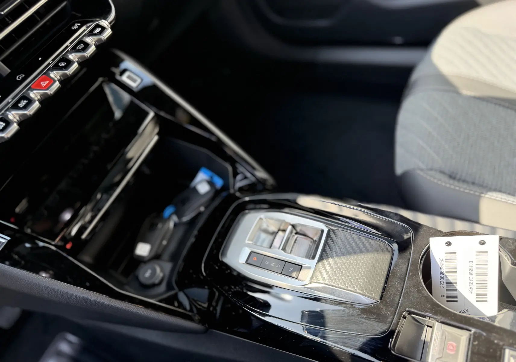 Gros plan sur la console centrale noire brillante avec levier de vitesses électronique et sièges tissu gris du Peugeot 2008 Hybrid 145ch.