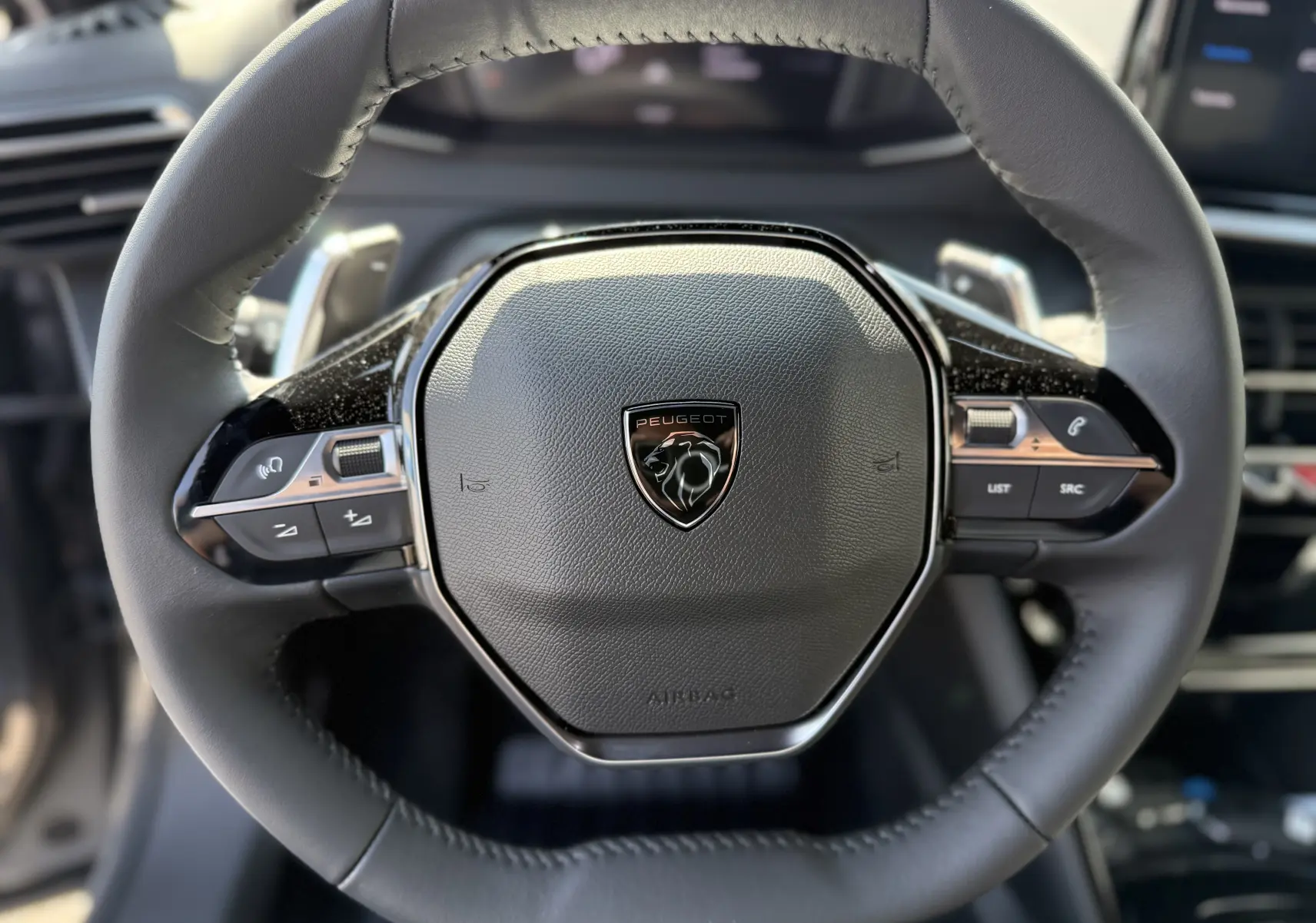 Gros plan sur le volant cuir noir du Peugeot 2008 Hybrid 145ch Allure 2025 avec commandes intégrées et logo lion central.