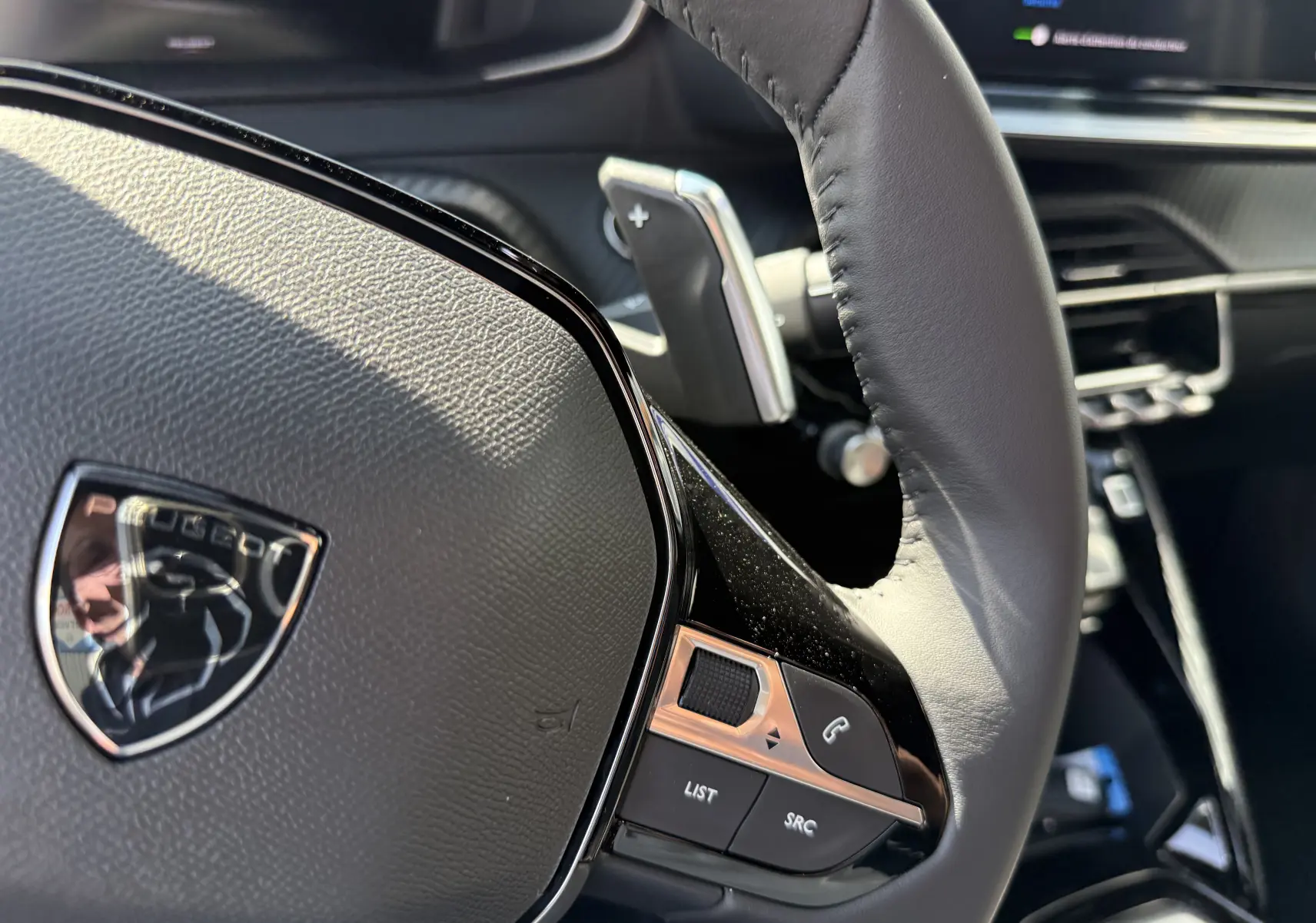 Gros plan sur le volant cuir gris du Peugeot 2008 Hybrid 145ch avec commandes intégrées et palettes au volant.