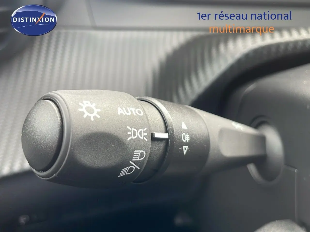 Gros plan sur la commande des phares du Peugeot 2008 2024, avec marquages blancs sur plastique noir texturé.