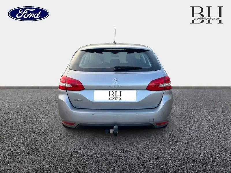 Vue arrière d'une Peugeot 308 SW gris Artense avec attelage visible sur un sol goudronné.