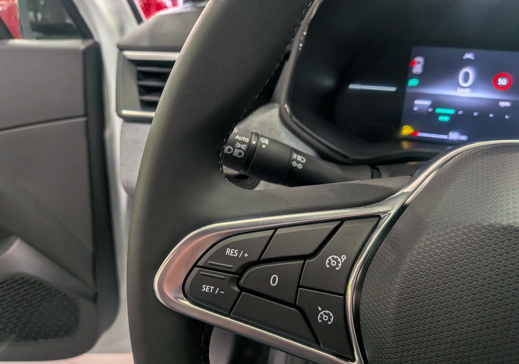 Gros plan sur le volant noir de la Renault Clio V blanc glacier, montrant les commandes de régulateur de vitesse côté gauche.