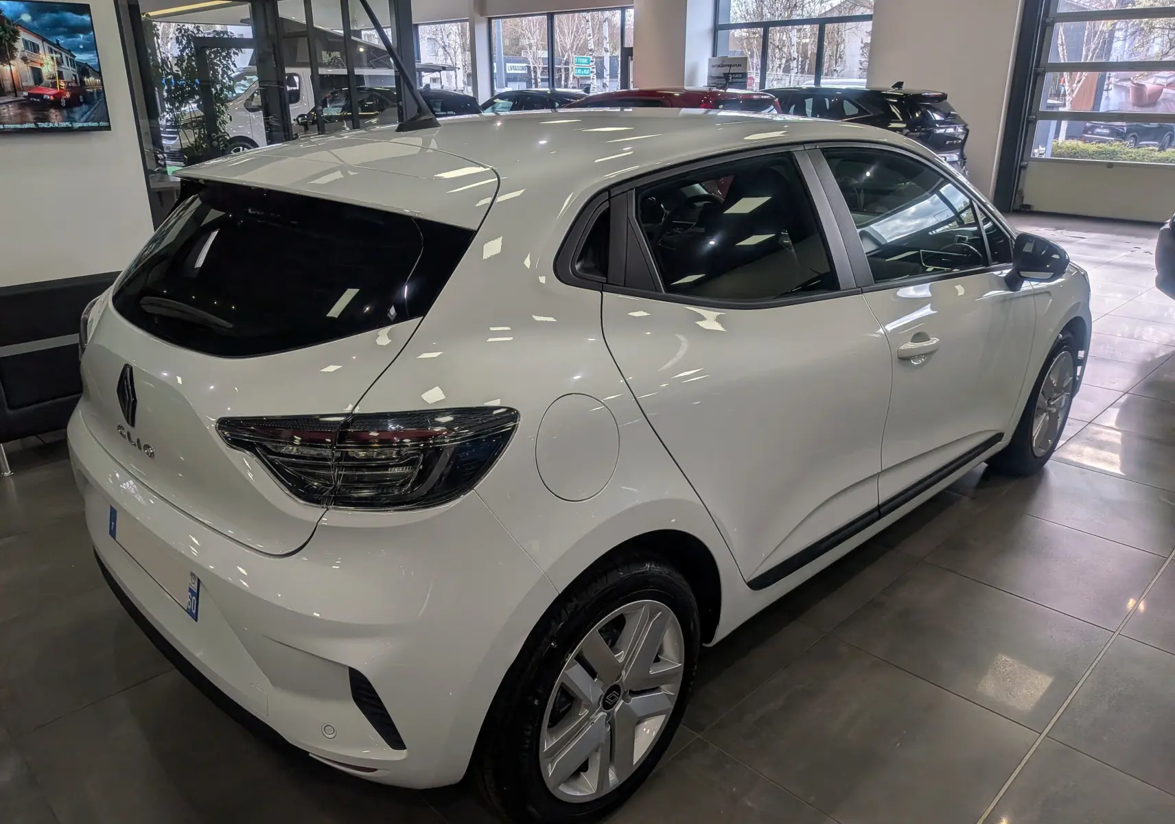 Renault Clio V Blue dCi 100 en Blanc Glacier vue 3/4 arrière droit en intérieur, feux arrière fumés et jantes alliage.