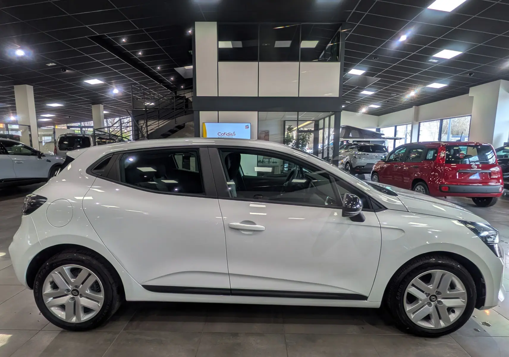 Profil côté gauche d'une Renault Clio V Blanc Glacier 2025 en showroom, soulignant ses lignes épurées et jantes alliage.