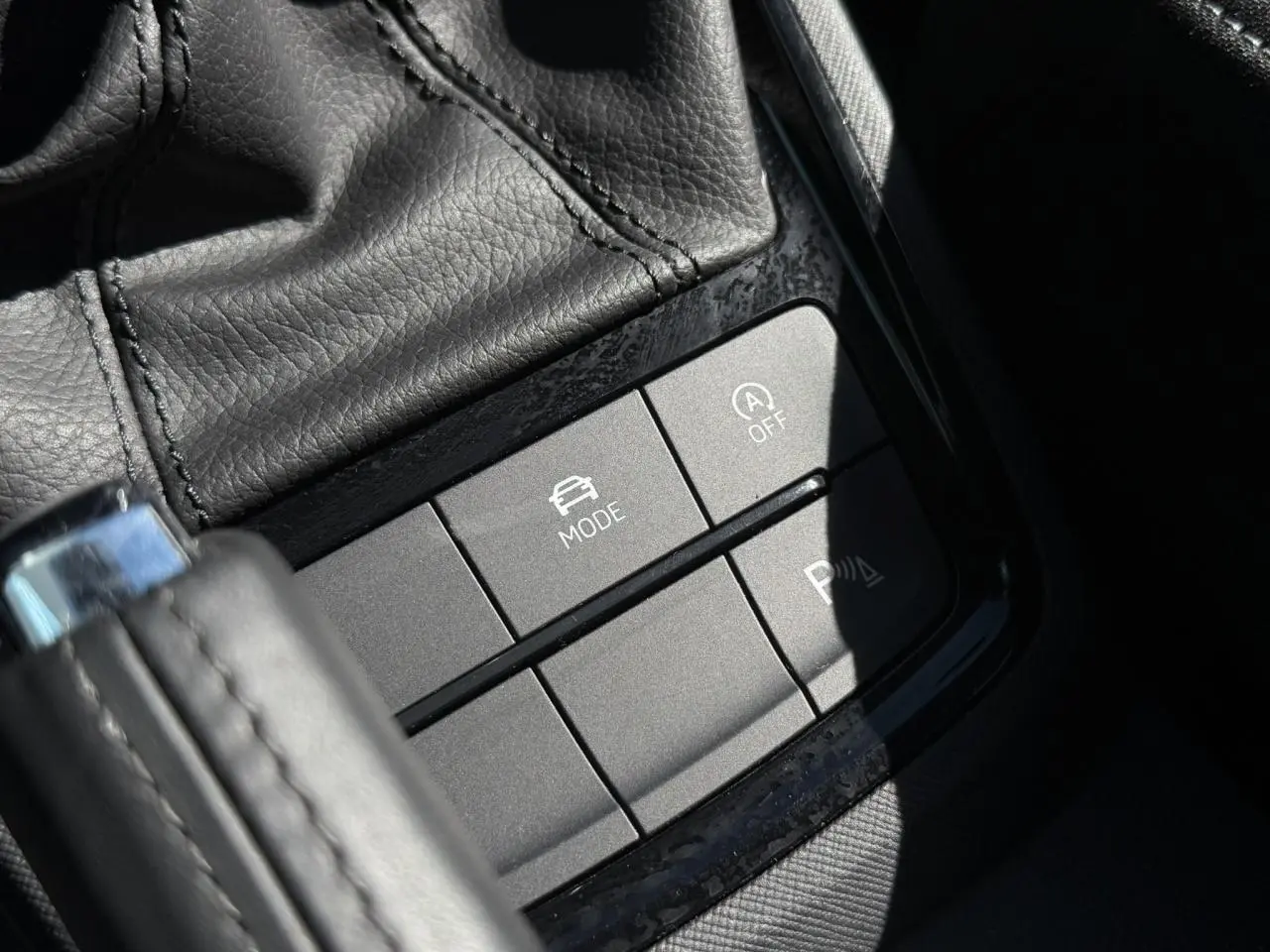 Gros plan sur les boutons de commande gris mat près du levier de vitesse en cuir noir dans une Skoda Scala Bleu Energy.