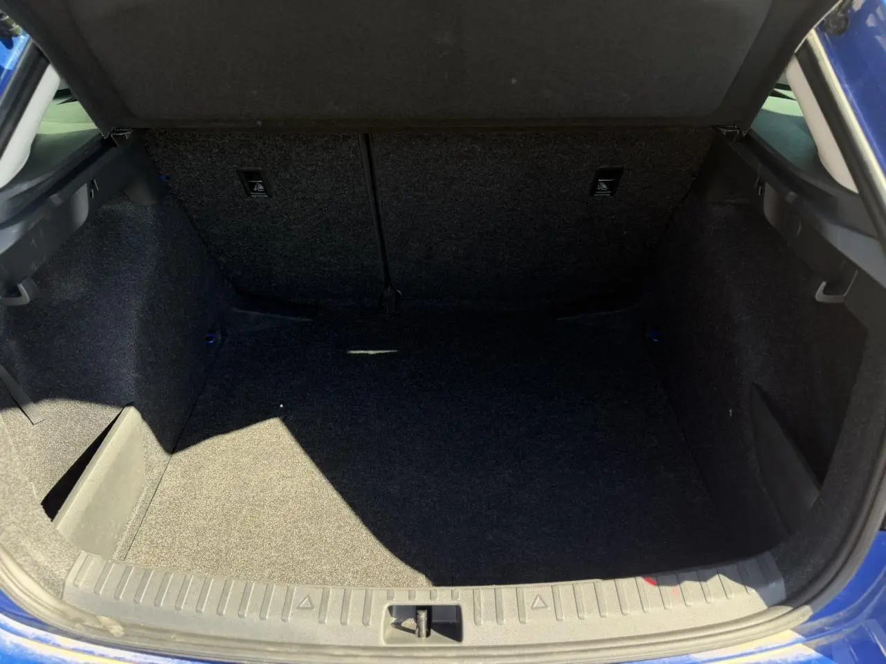 Coffre ouvert vu de l'arrière d'une Skoda Scala TSI 116 DSG7 bleu Energy, espace de chargement vide et propre.