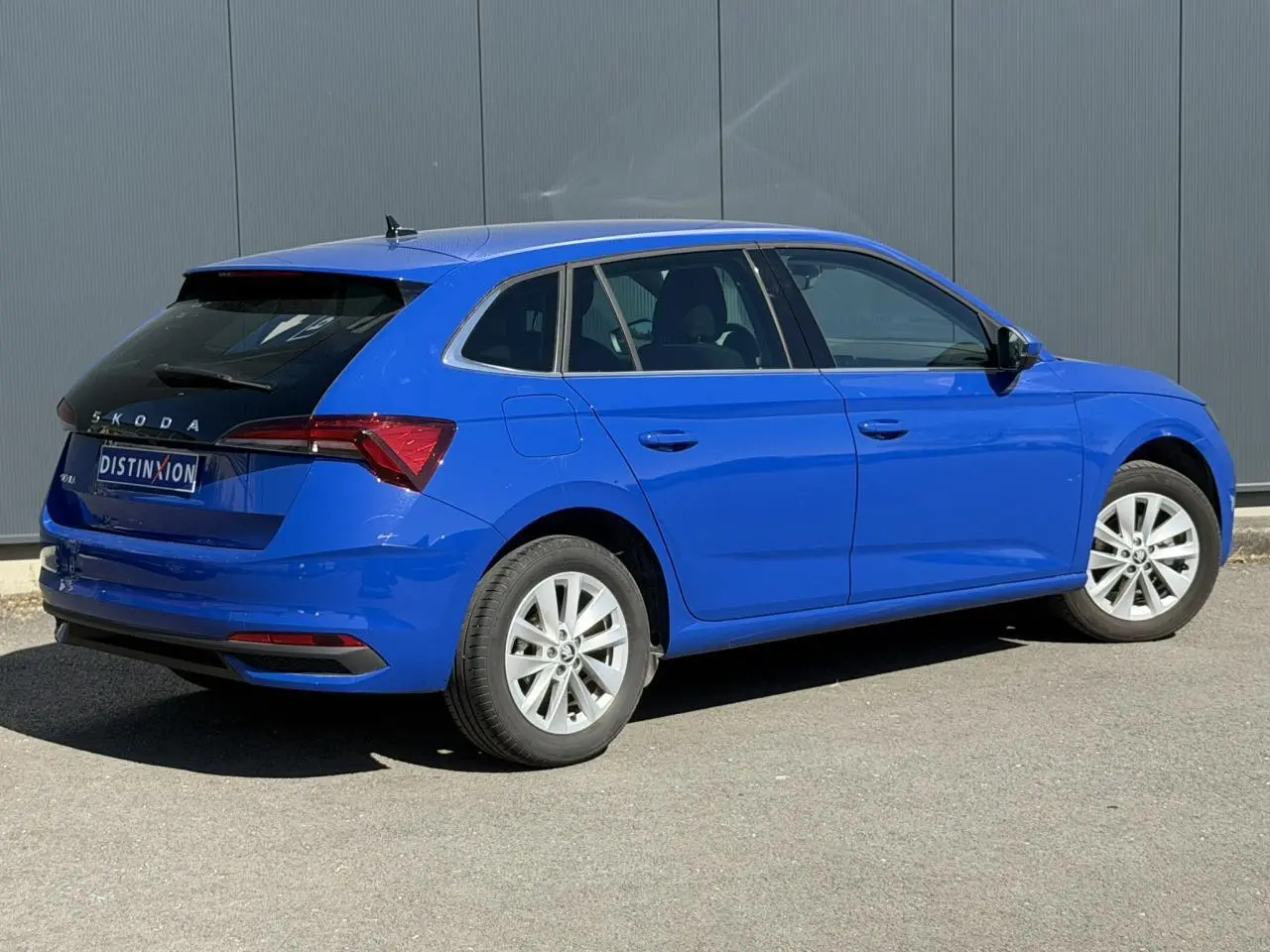Vue 3/4 arrière droite d'une Skoda Scala bleu Energy avec vitres arrière surteintées et jantes alliage 16 pouces.