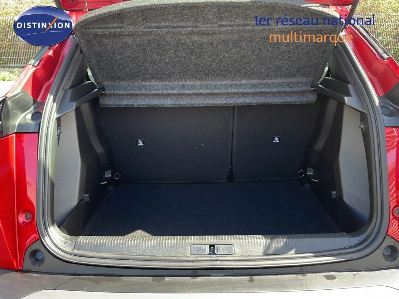 Coffre ouvert vu de l'arrière d'une Peugeot 2008 rouge Elixir Metal, montrant un espace de chargement vide et propre.