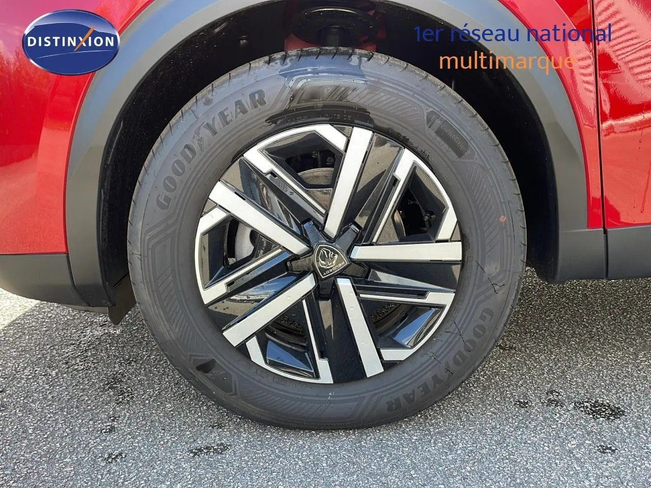 Gros plan sur la roue avant droite d'un Peugeot 2008 rouge Elixir Metal avec jante alliage bicolore moderne.