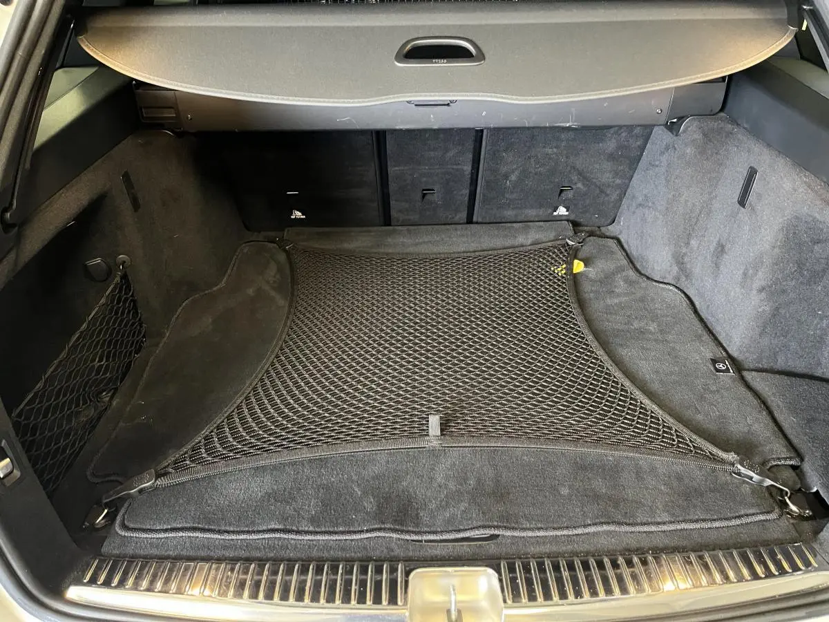 Coffre ouvert d'un Mercedes Classe C Break blanc, vue intérieure avec filet de rangement noir et tapis de sol.